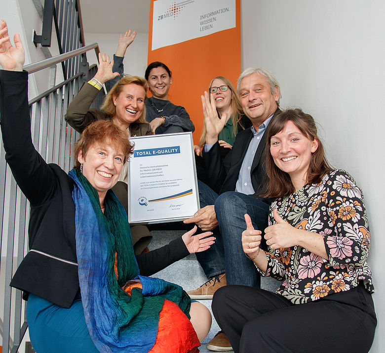 Direktion, Gleichstellungsbeauftragte und Personalabteilung von ZB MED halten die Urkunde zur Verleihung des TOTAL E-QUALITY-Prädikats hoch und freuen sich über die Auszeichnung.