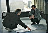 Ulricht Korwitz, ehemaliger Direktor von ZB MED, betrachtet gemeinsam mit einem Architekten große Baupläne, die auf dem Boden liegen.